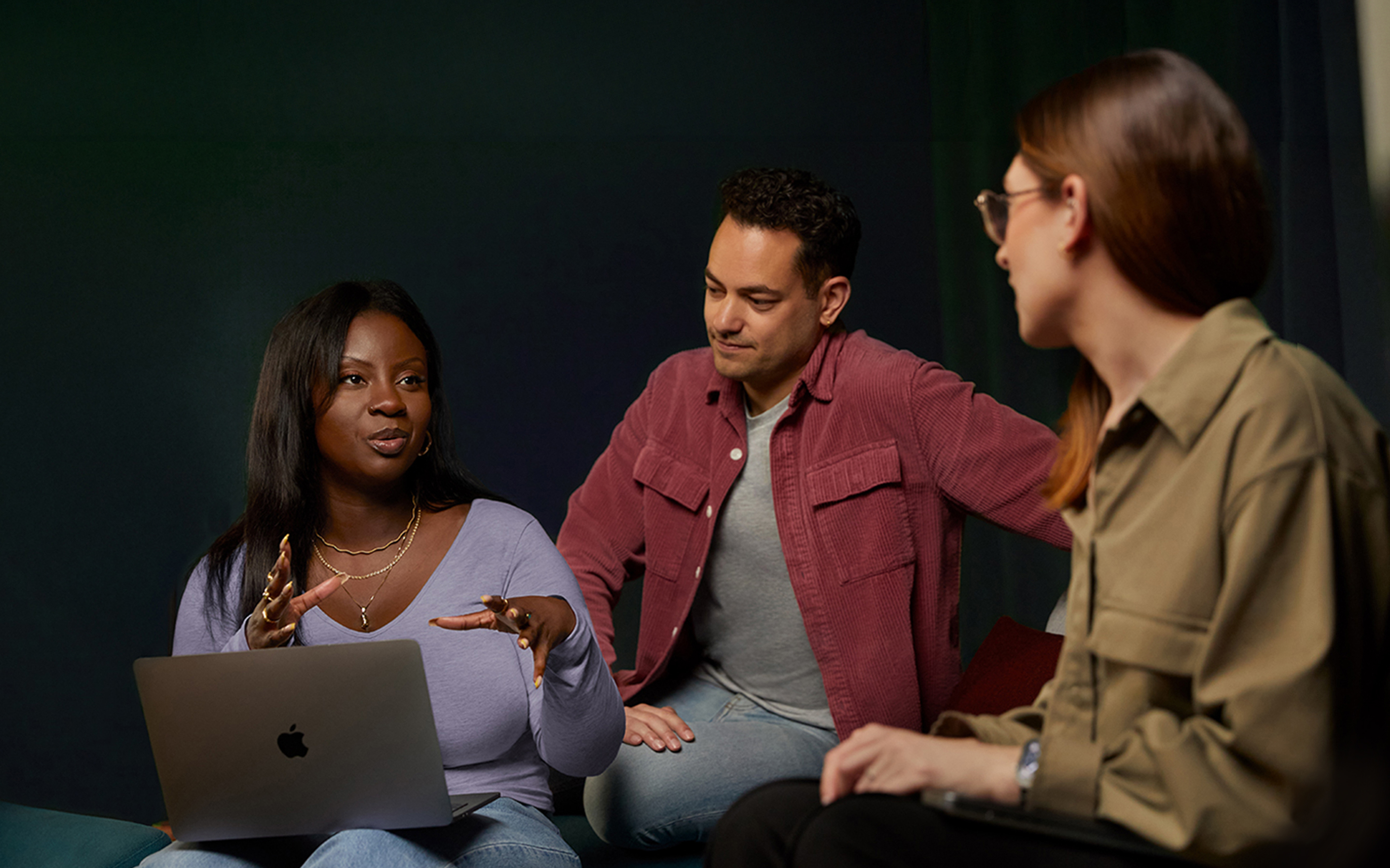 Tres personas del equipo de software y servicios de Apple conversan en un sofá, una de ellas con un MacBook.