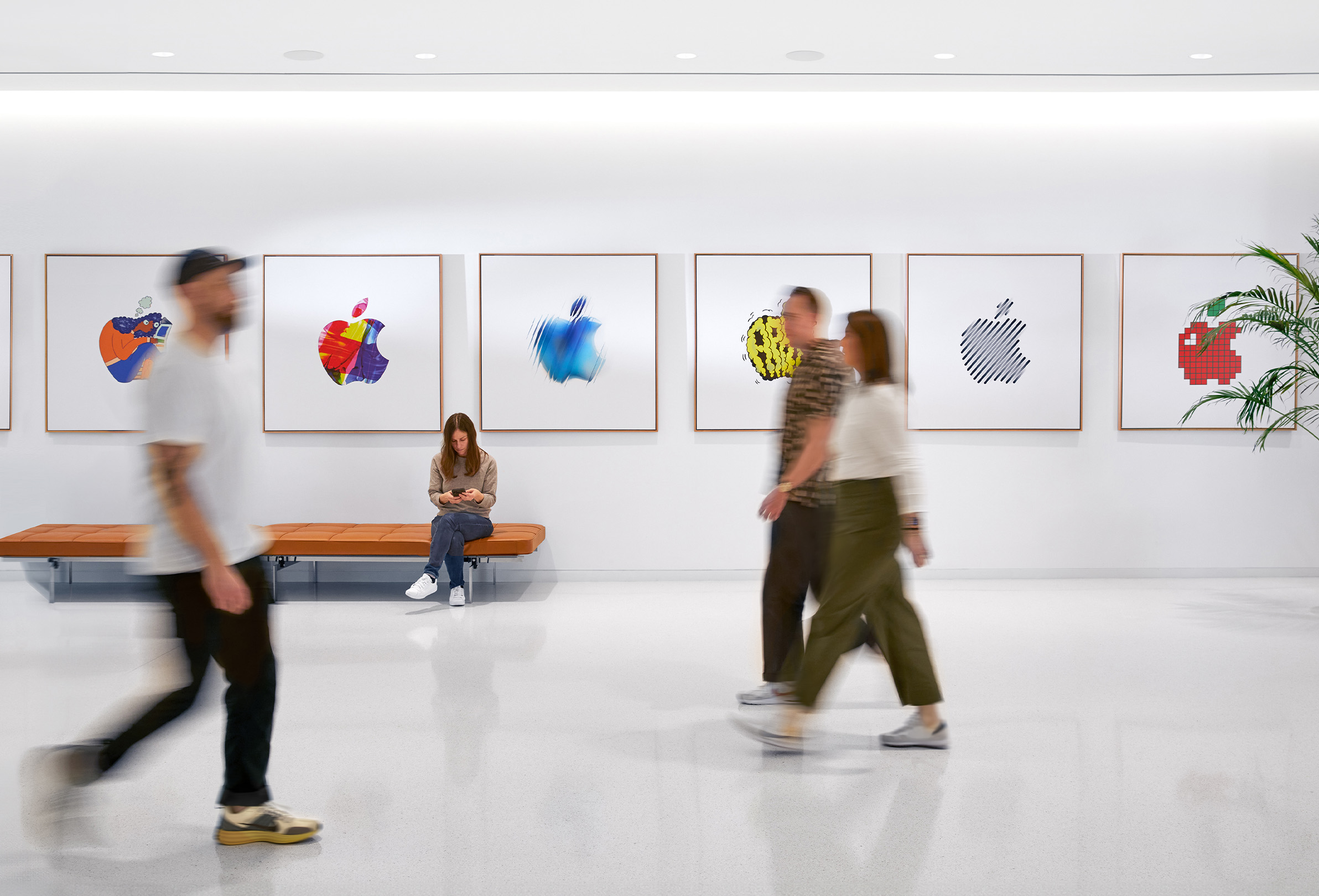 Drie Apple medewerkers die langs een binnenwand met kleurrijke Apple logo’s lopen. Een vierde medewerker zit op een bank.