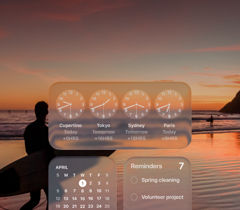 Liquid Glass kell, kalender, meeldetuletused ja ilmarakendus macOS Tahoe ekraanil, mille taustal on stseen surfarist, kes jalutab päikseloojangul rannas