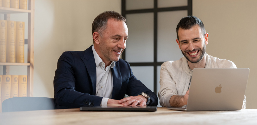 Twee mannen werken samen en kijken naar een geopende MacBook.