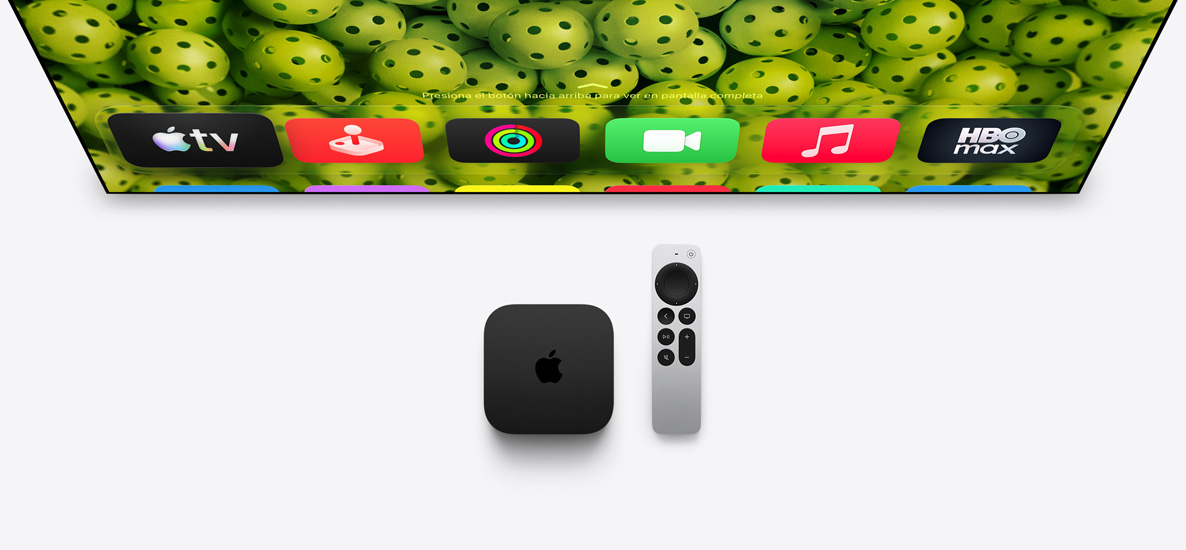 Un Apple TV 4K y un control Siri Remote debajo de un televisor, la pantalla muestralos íconos de las apps de la pantalla de inicio en la fila superior sobre un fondo verde con pelotas de pickleball