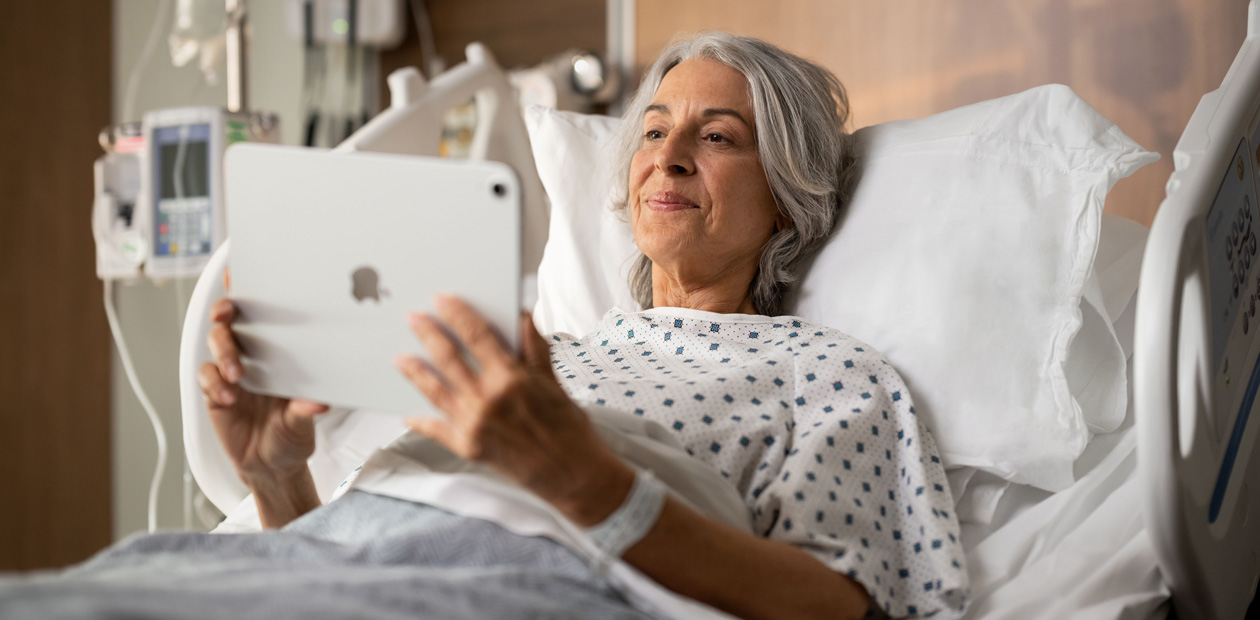 En kvindelig patient ligger i en hospitalsseng, mens hun kigger på sin iPad.