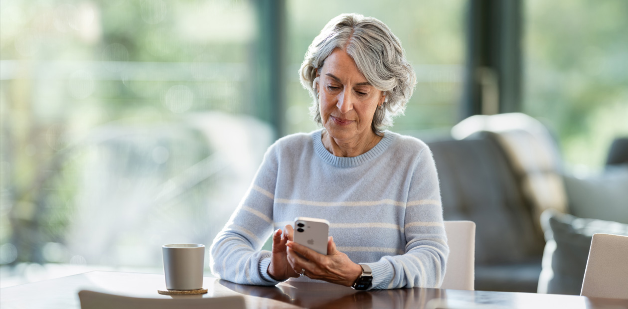 Una anciana mira un iPhone sentada a una mesa.