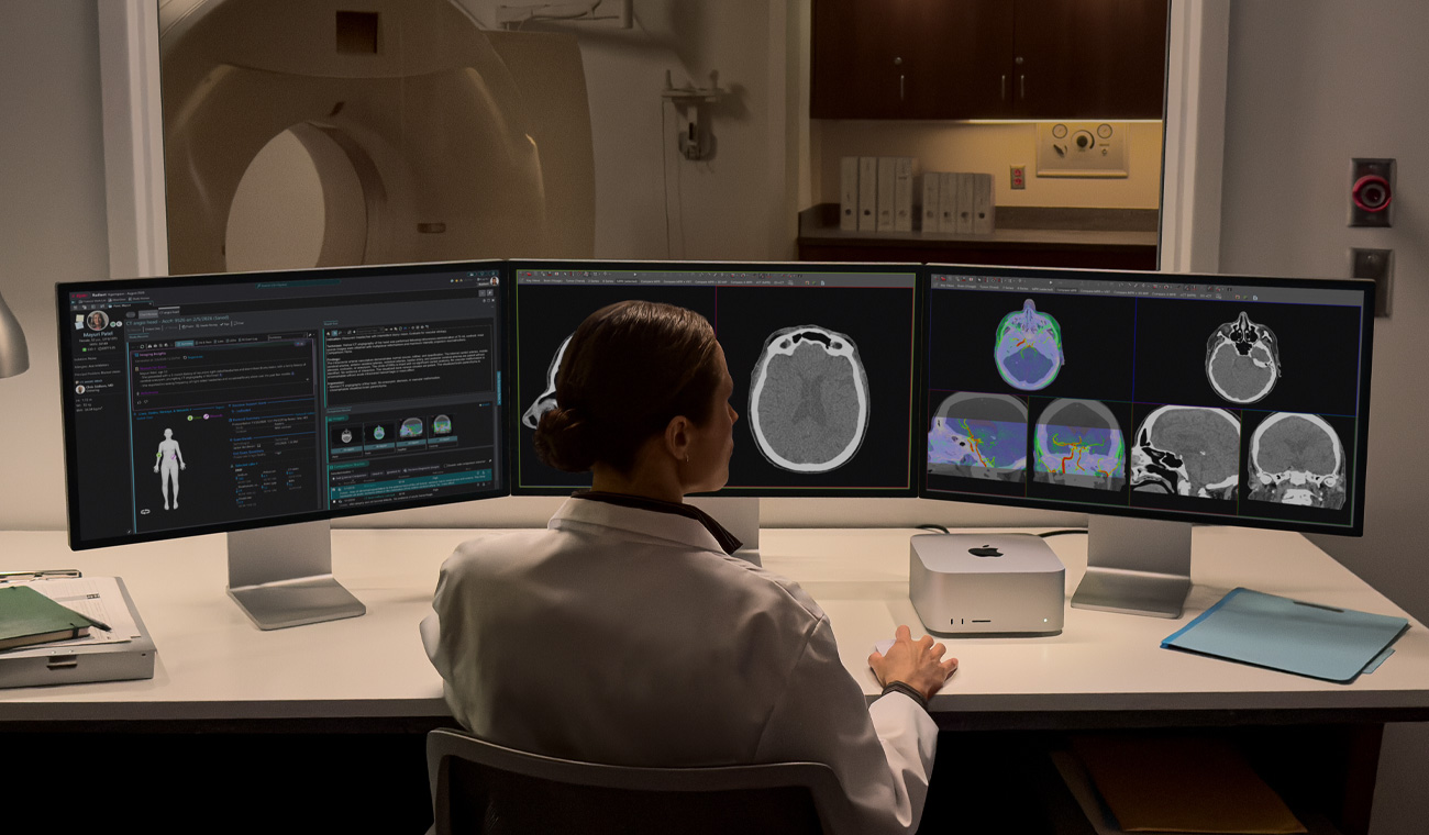 Une personne est assise à un bureau sur lequel se trouvent trois Studio Display côte à côte et un Mac Studio, tous les écrans affichent des applications d’imagerie médicale