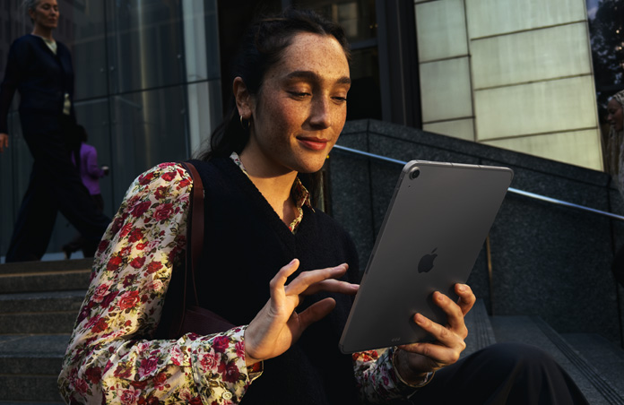 Une personne assise sur des marches devant un grand immeuble utilise un iPad Air 11 pouces gris cosmique, dont la connexion Wi-Fi reste stable pendant le transfert réseau