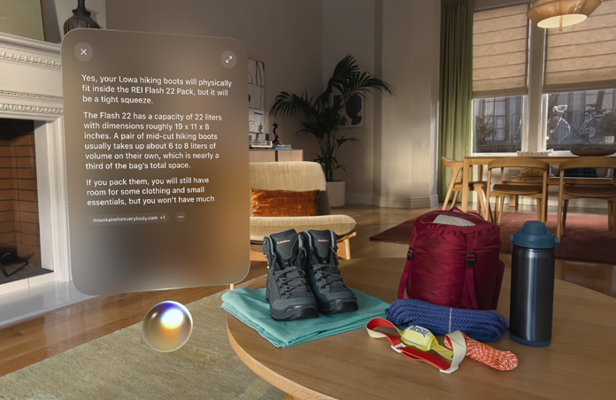 Écran affichant la réponse à une requête Siri sur les essentiels de camping, flottant au-dessus de la bulle Siri sur le côté gauche, avec des chaussures de randonnée, des cordes, un sac à dos, une bouteille d’eau et une lampe frontale posés sur une table sur le côté droit
