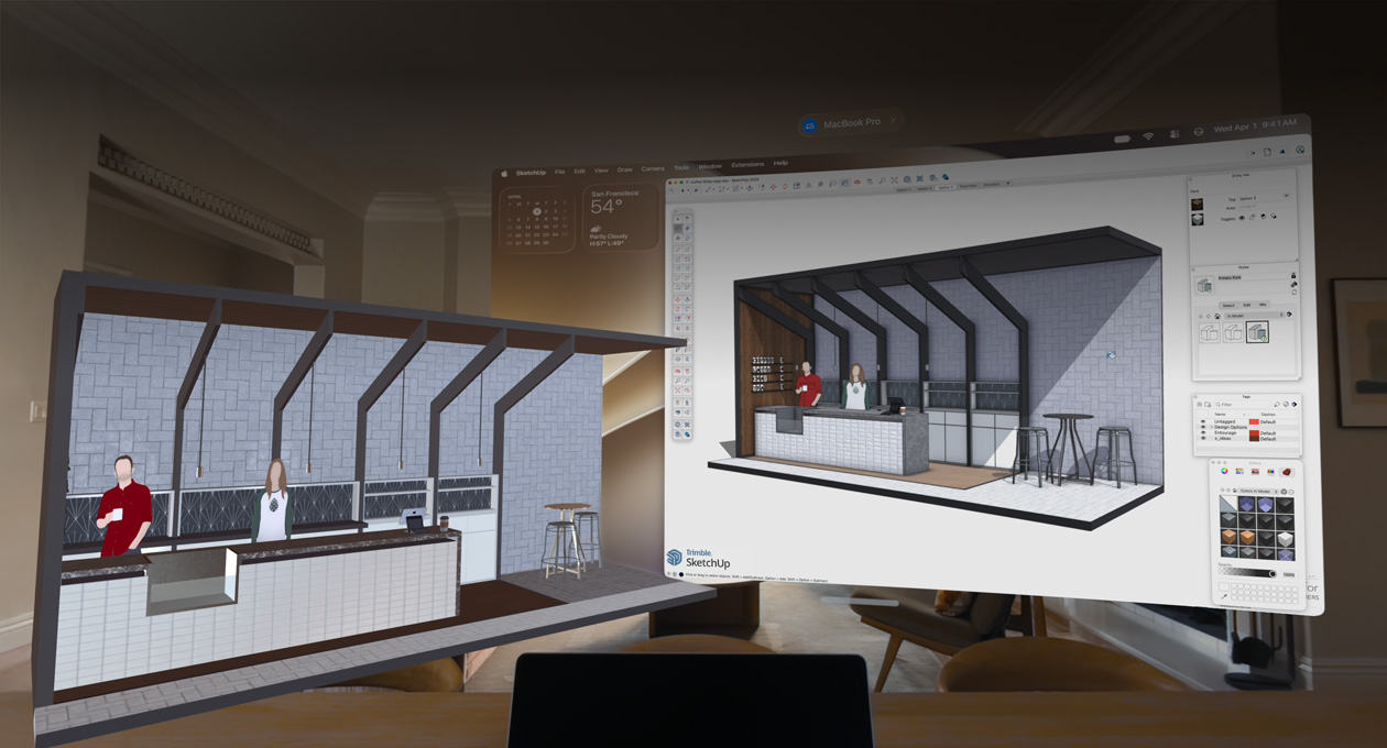 Vue d’un Apple Vision Pro, un MacBook Pro est posé sur une surface avec des modèles 3D projetés à l’arrière ; les modèles représentent un comptoir de café avec deux personnes debout derrière